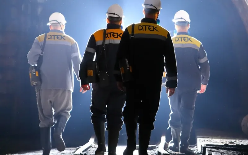 Miners in helmets and headlamps walking along an underground drift